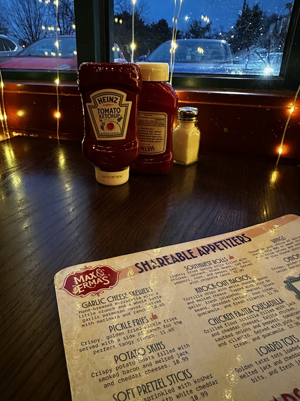 Menu for restaurant on wooden table. Condiment bottles are on the far end of table near window.