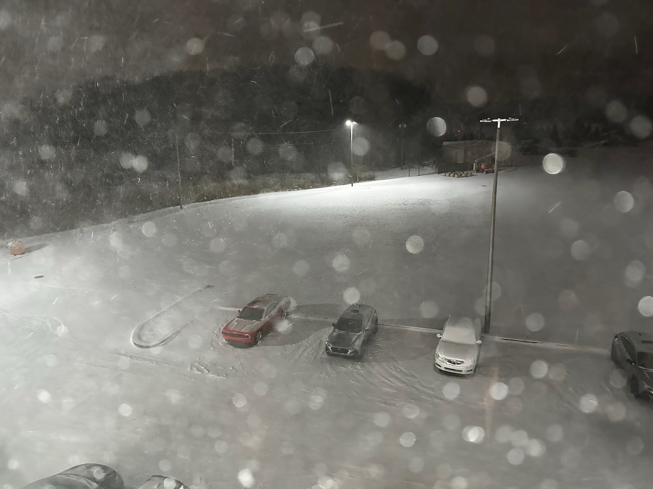 Snowstorm, with snow-covered parking lot of hotel in background.