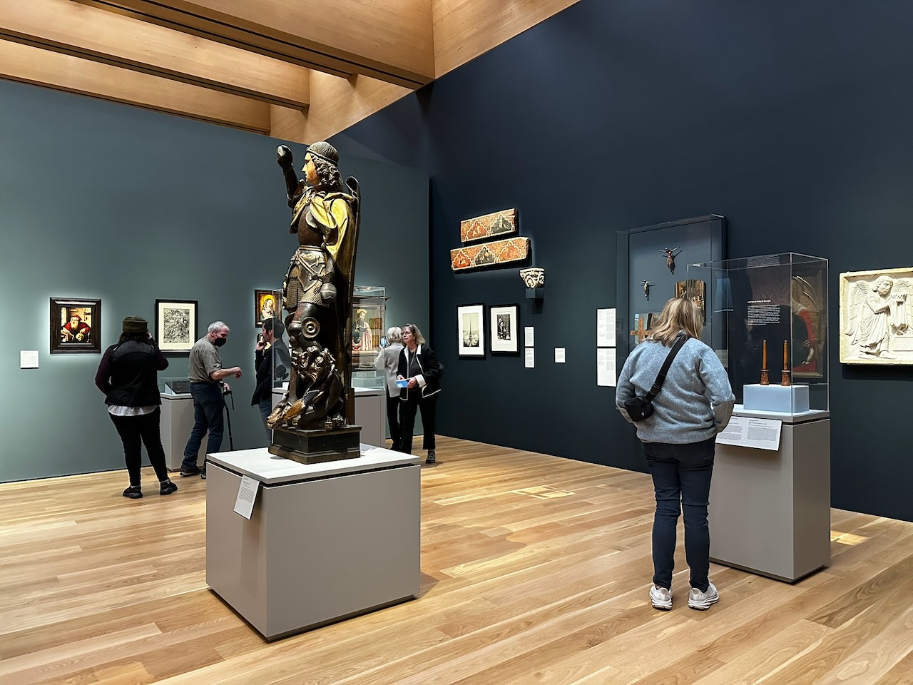Gallery in museum with people looking at exhibits of medieval sculptures and paintings.
