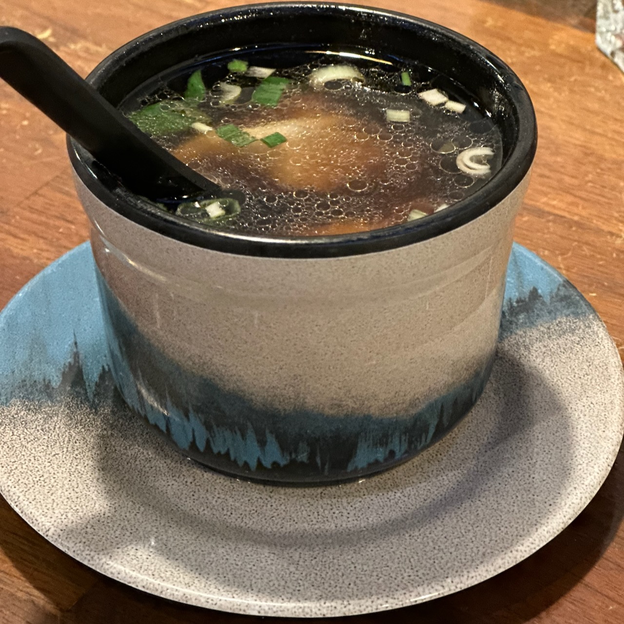 Cup of wonton soup on table.