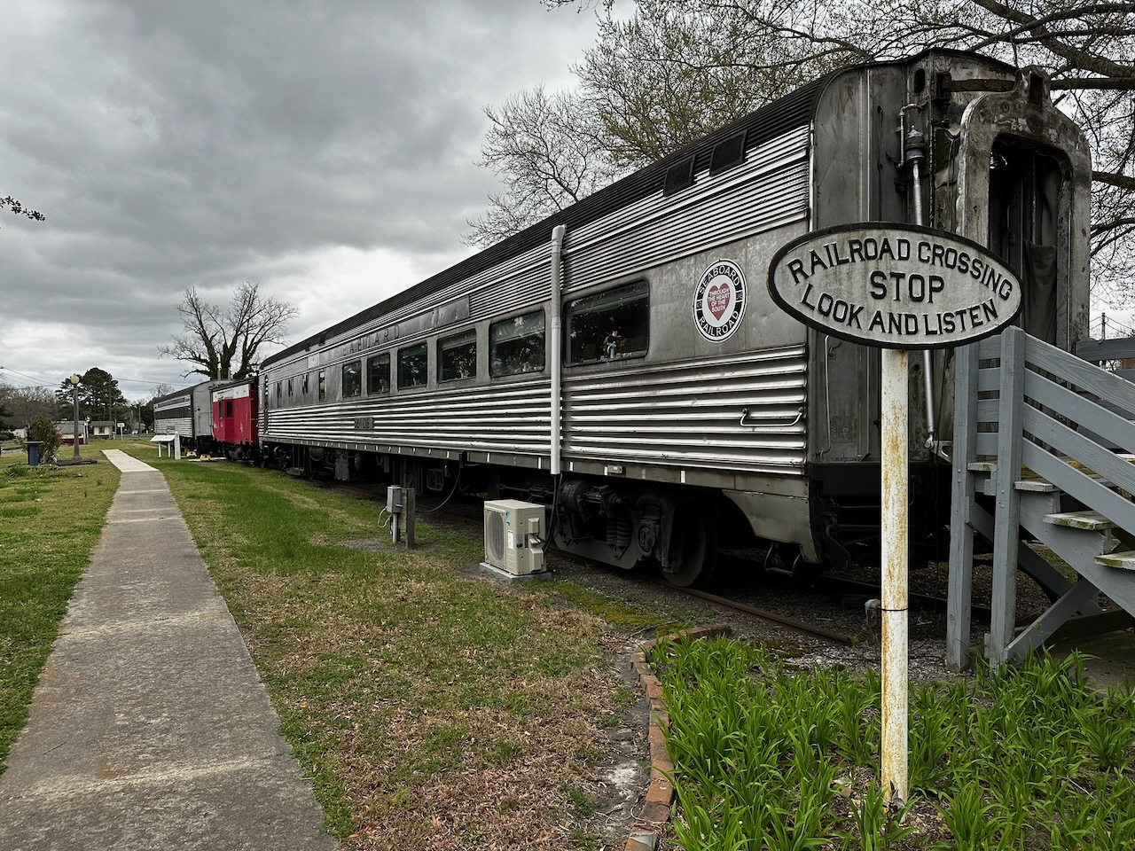 Dining passenger car with sign RAILROAD CROSSING STOP LOOK AND LISTEN in foreground.