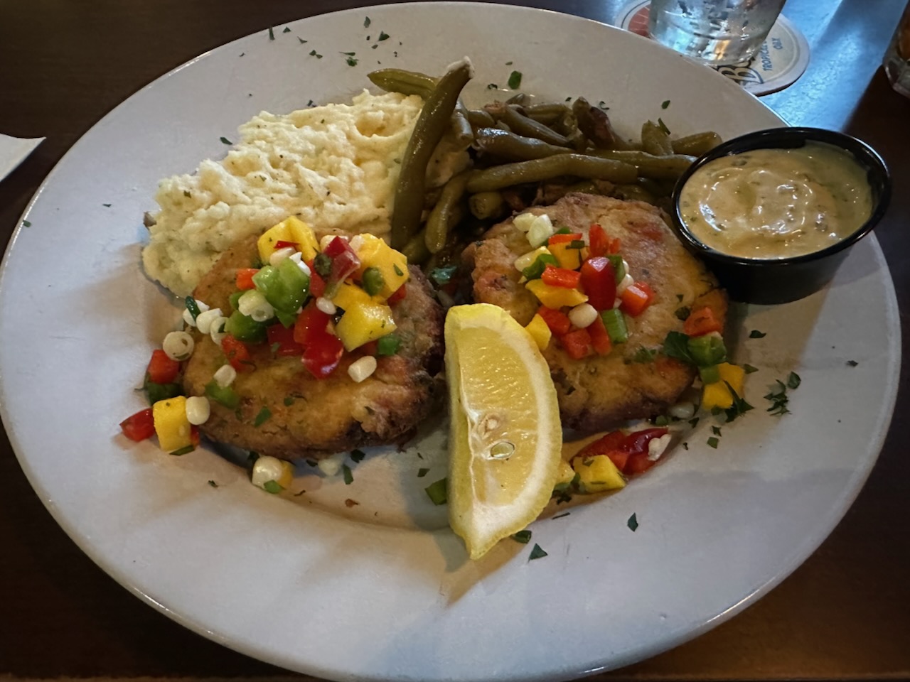 Crab cakes on white plate, with sides of mashed potatoes and string beans.