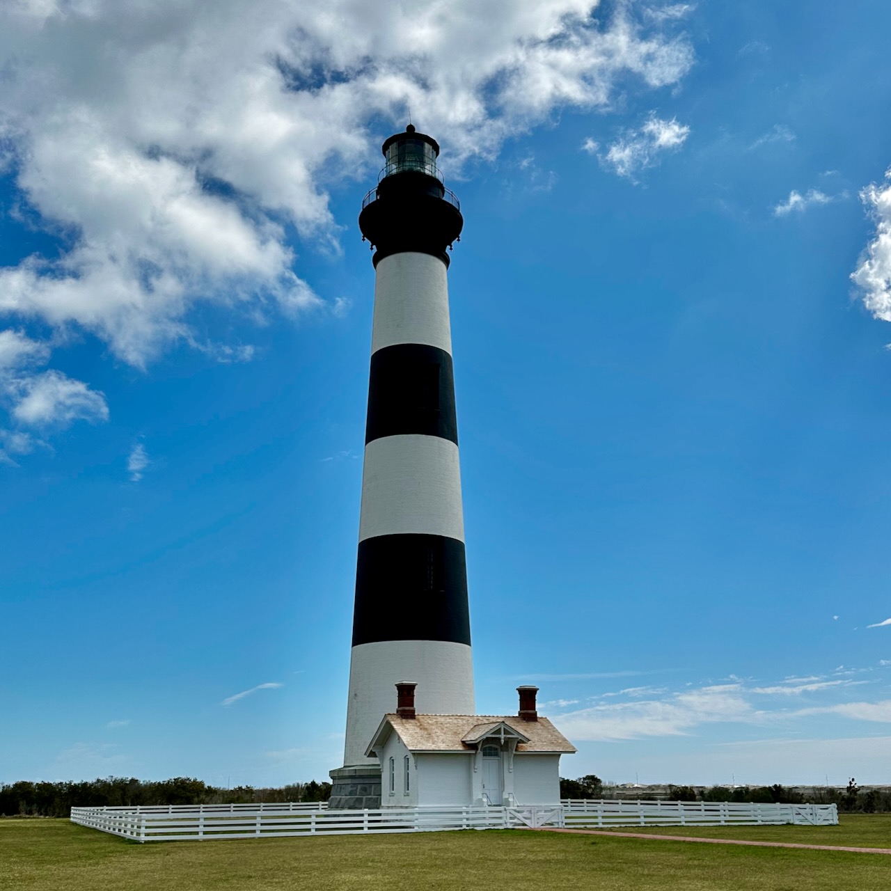 Bodie Island Light Station under a blue sky with a few clouds.