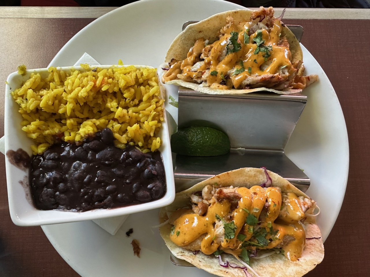 Fish tacos on white plate with beans and rice in white bowl.