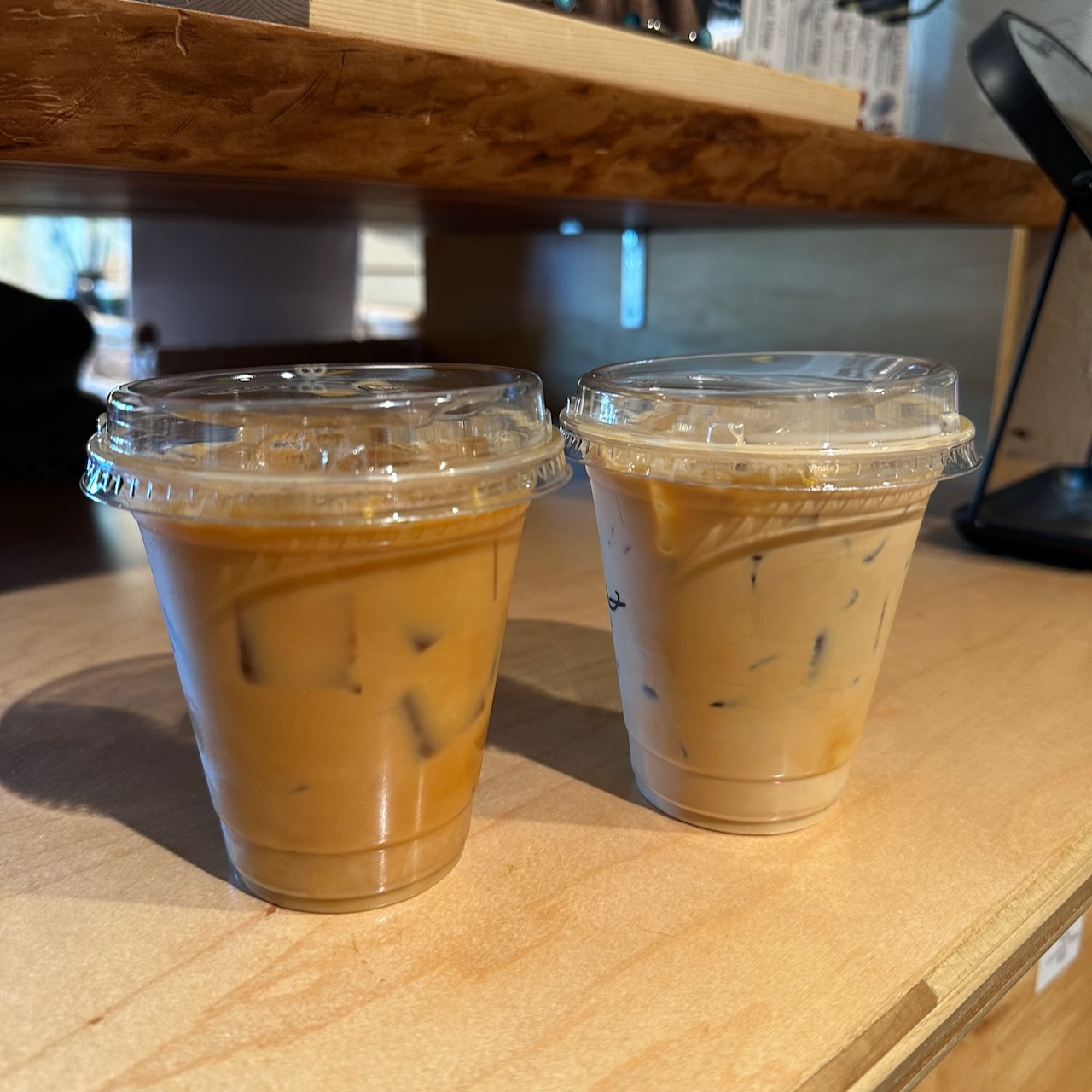Two iced lattes in clear plastic cups on counter.