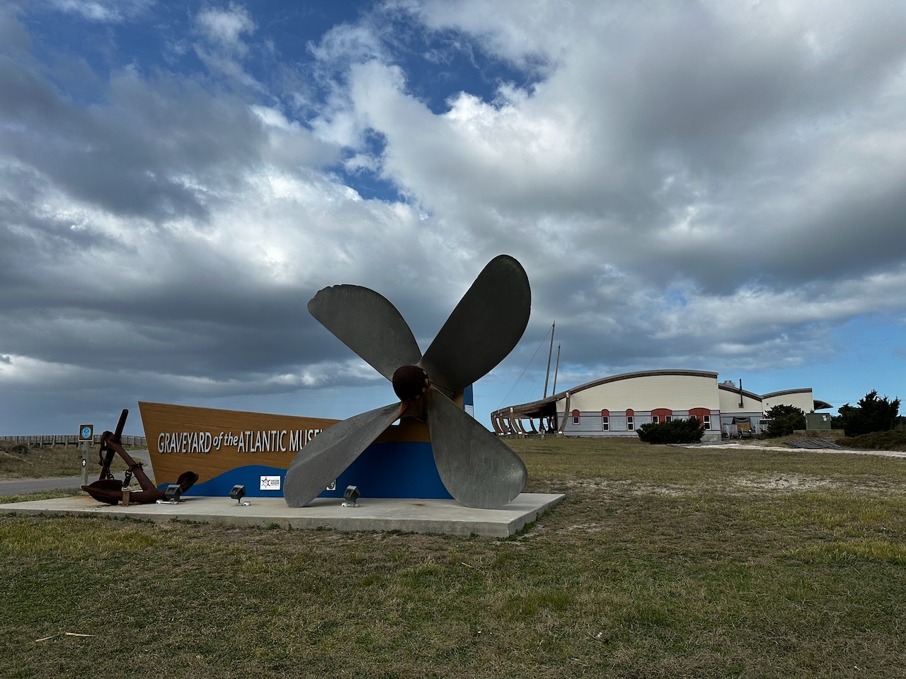 Graveyard of the Atlantic Museum sign and large propeller on lawn in front of museum.