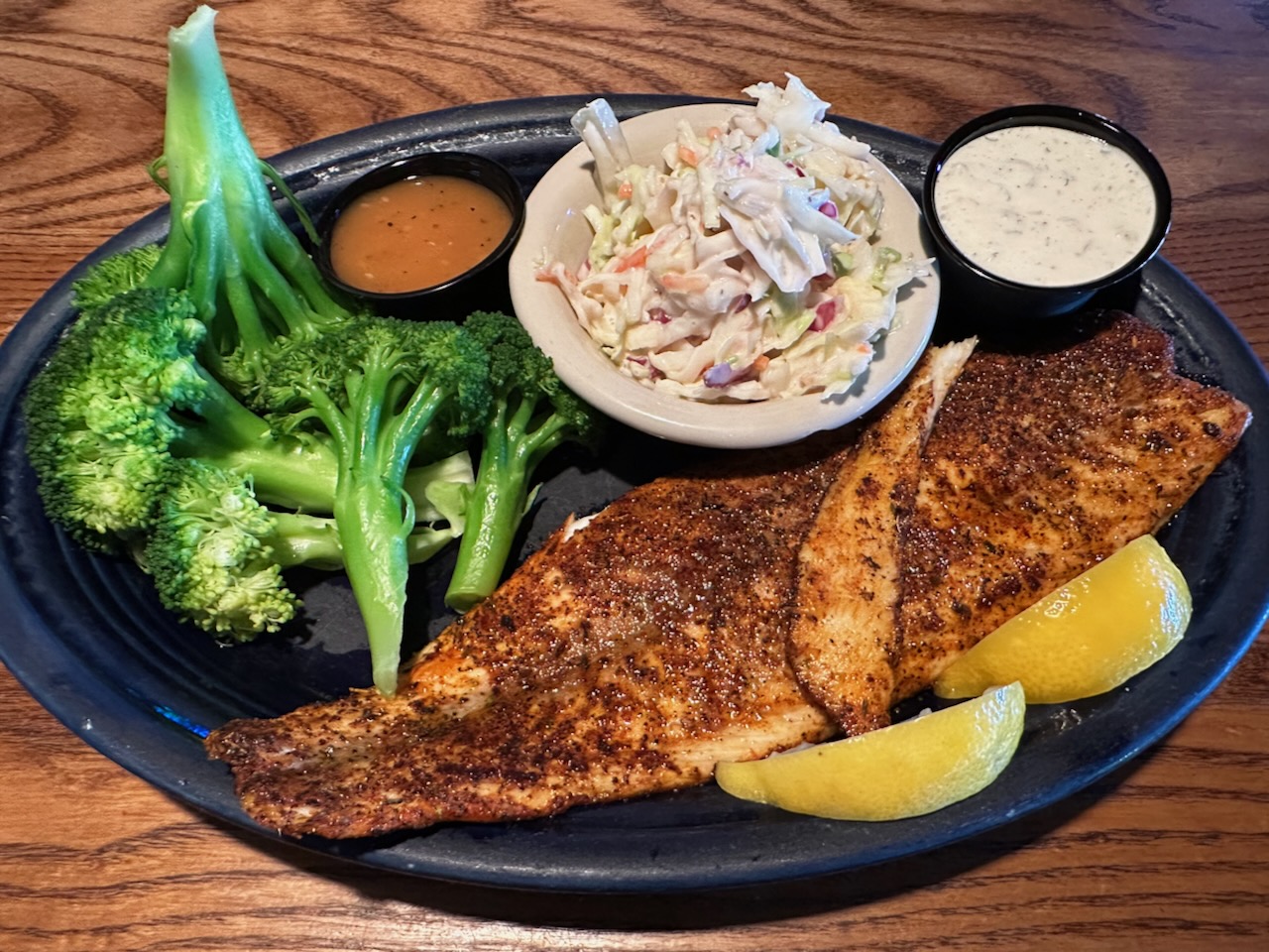 Seasoned drum fish on plate with sides of broccoli and coleslaw.