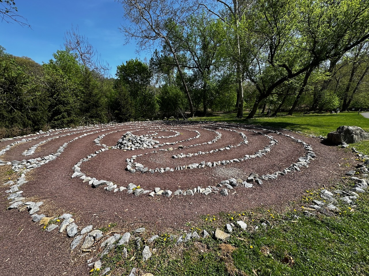 Stone labyrinth on ground, with line of trees in background.