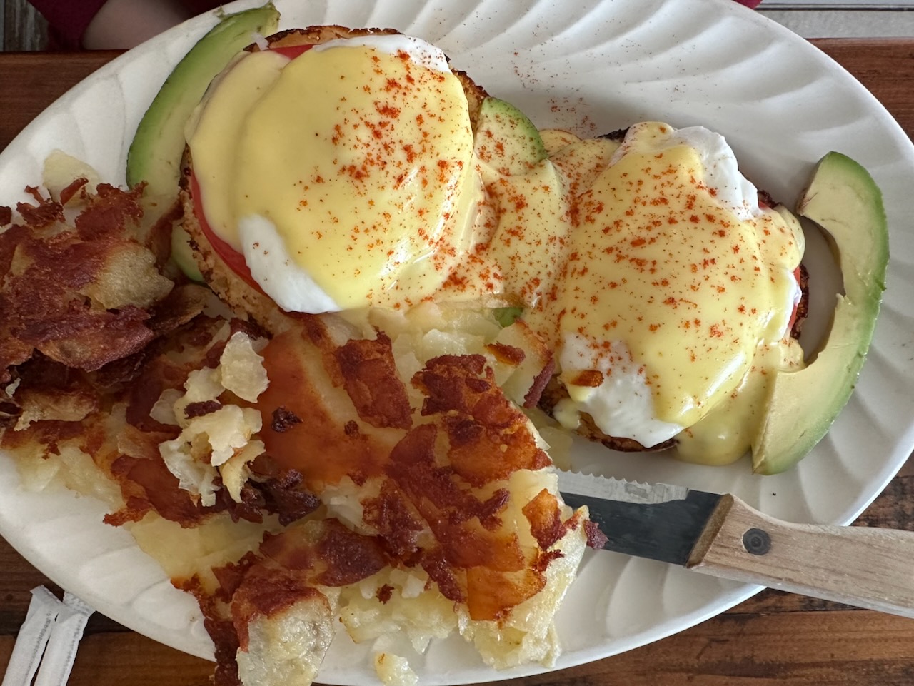 Eggs Benedict with side of home fries on white plate.