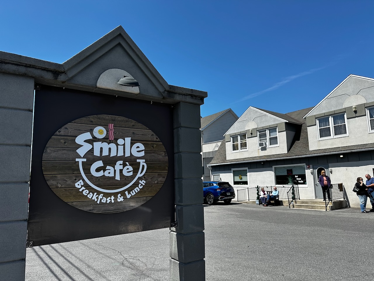 Wooden sign that says SMILE CAFE with restaurant in background.